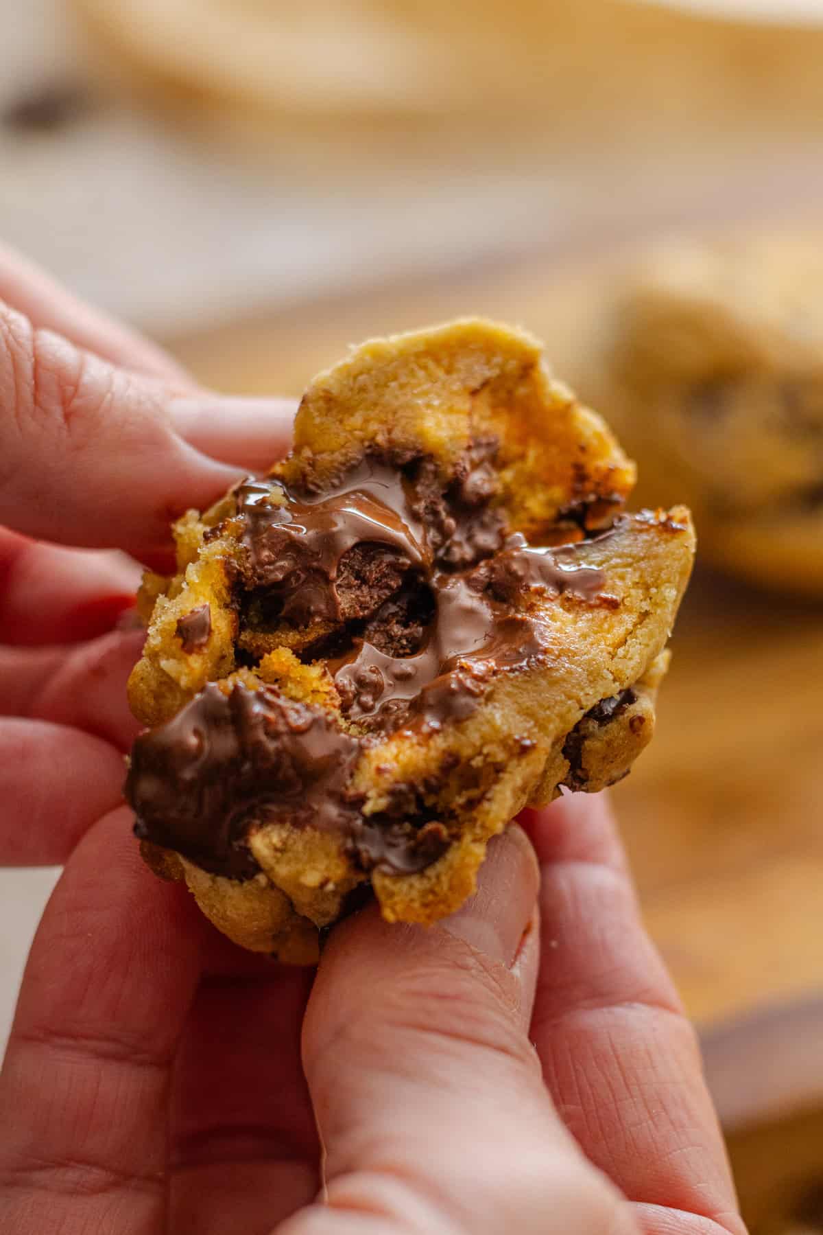 A hand breaking a gooey chocolate chip cookie in half to show the inside