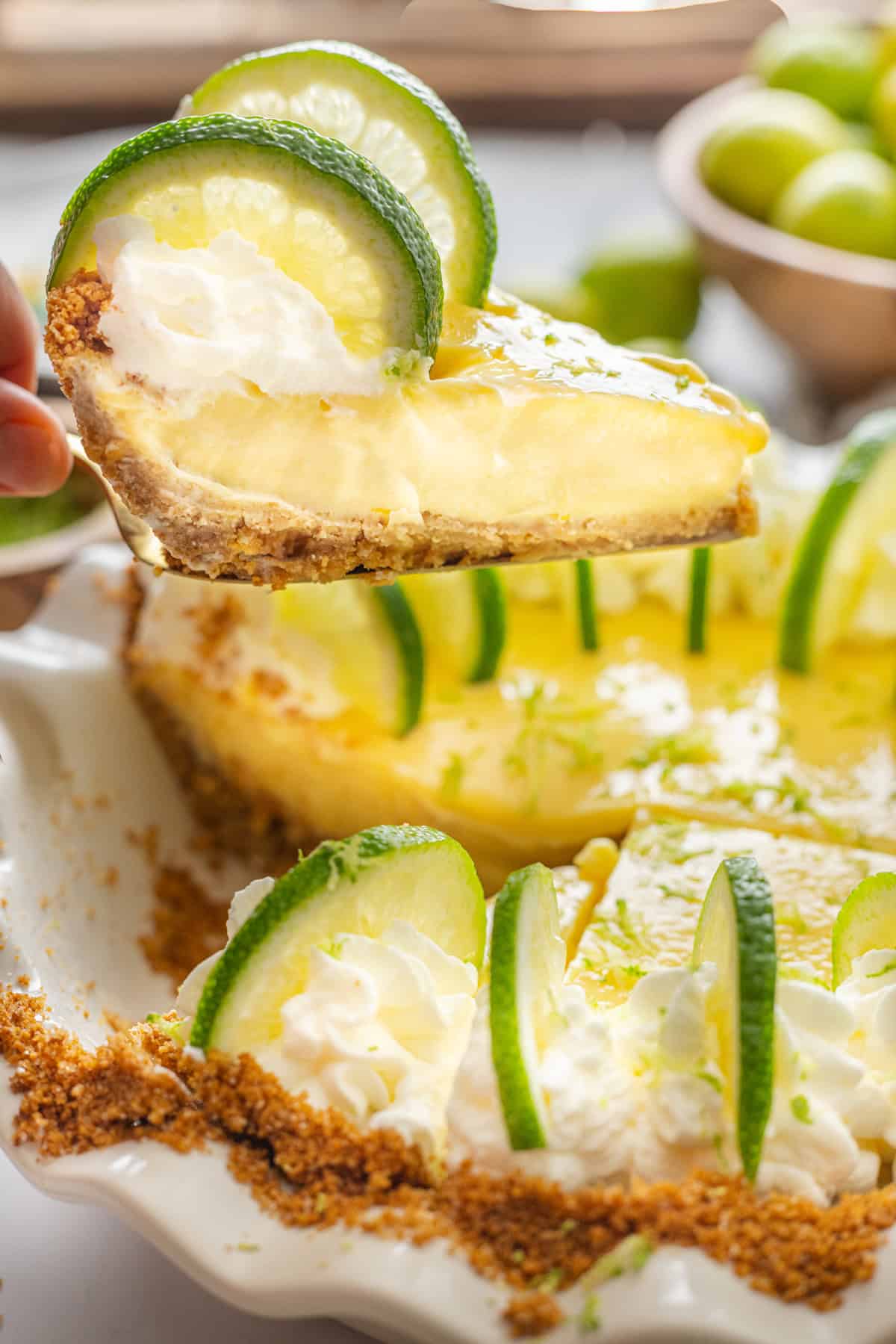 With a smooth, creamy filling in a graham cracker crust, this Key Lime Pie is infused with tangy citrus flavor. Super easy to make! A slice of key lime pie on a spatula above the pie