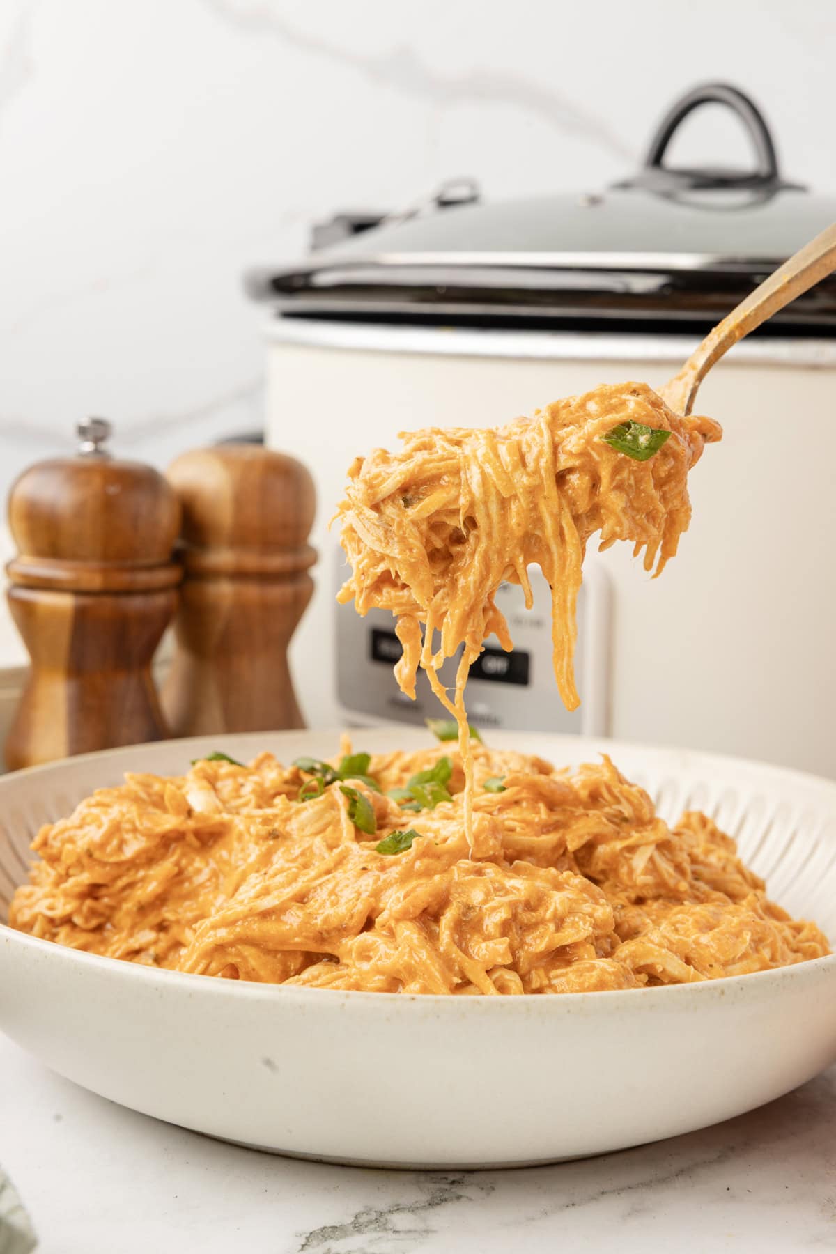 A bite of slow cooker buffalo chicken on a fork over a bowl