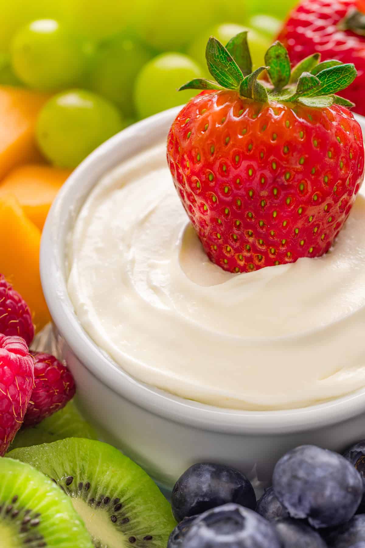 Light and creamy, this 2-Ingredient Fruit Dip is the perfect treat for summer! Serve with fresh fruit for a quick and easy dessert. A strawberry in a dish of fruit dip