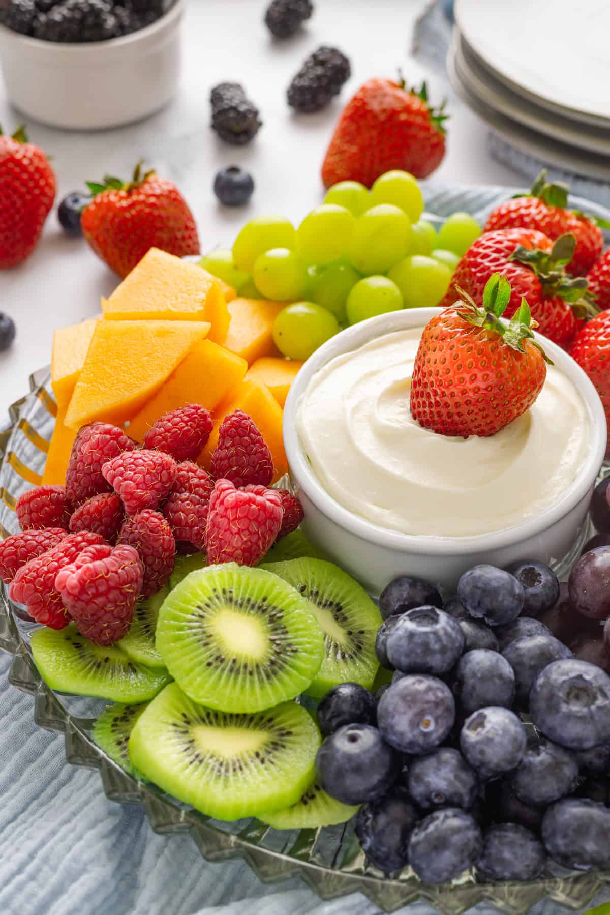 Light and creamy, this 2-Ingredient Fruit Dip is the perfect treat for summer! Serve with fresh fruit for a quick and easy dessert. A bowl of fruit dip with a strawberry surrounded by other fruit