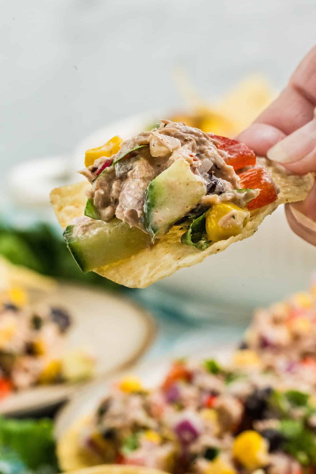 A hand holding a tortilla chip with Mexican tuna salad