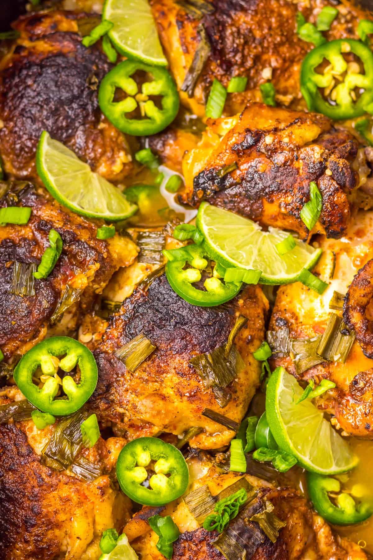 Close up of slow cooker jerk chicken topped with lime wedges and jalapeno slices