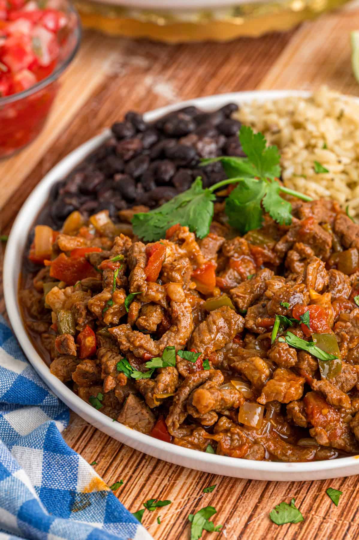 This Carne Picada recipe features braised beef and veggies in a rich, savory sauce. Serve with rice and beans or in tacos and burrito bowls. A plate of carne picada with black beans and rice