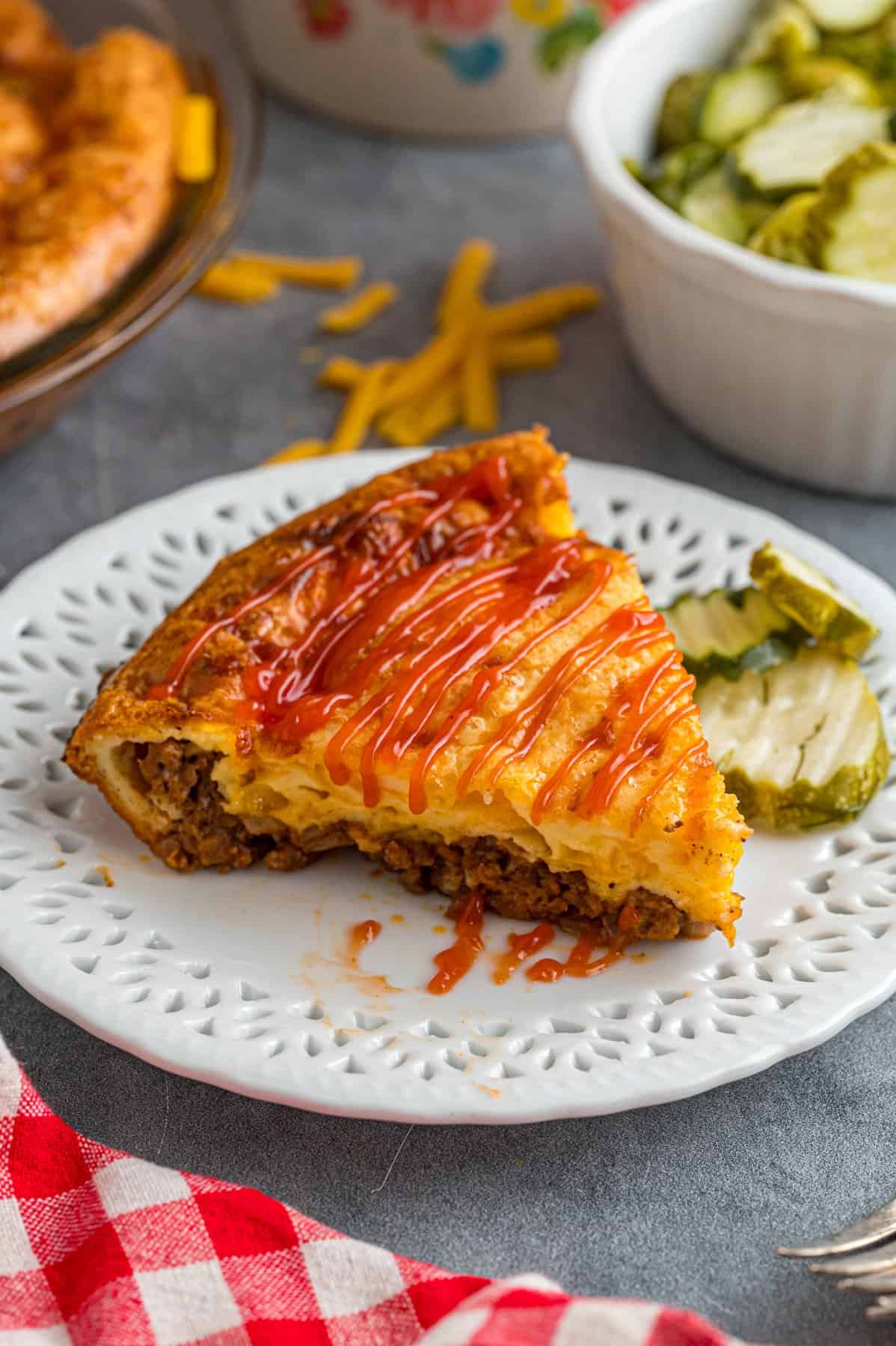 A slice of cheeseburger pie on a plate with pickles