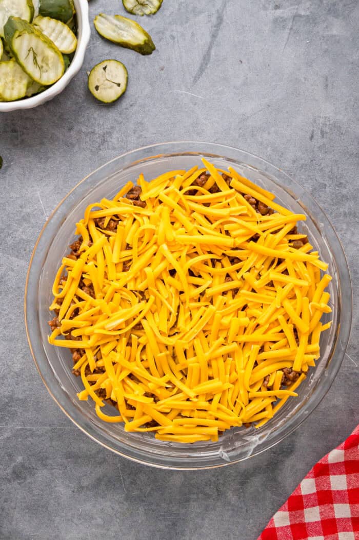Shredded cheddar on top of ground beef in a pie dish