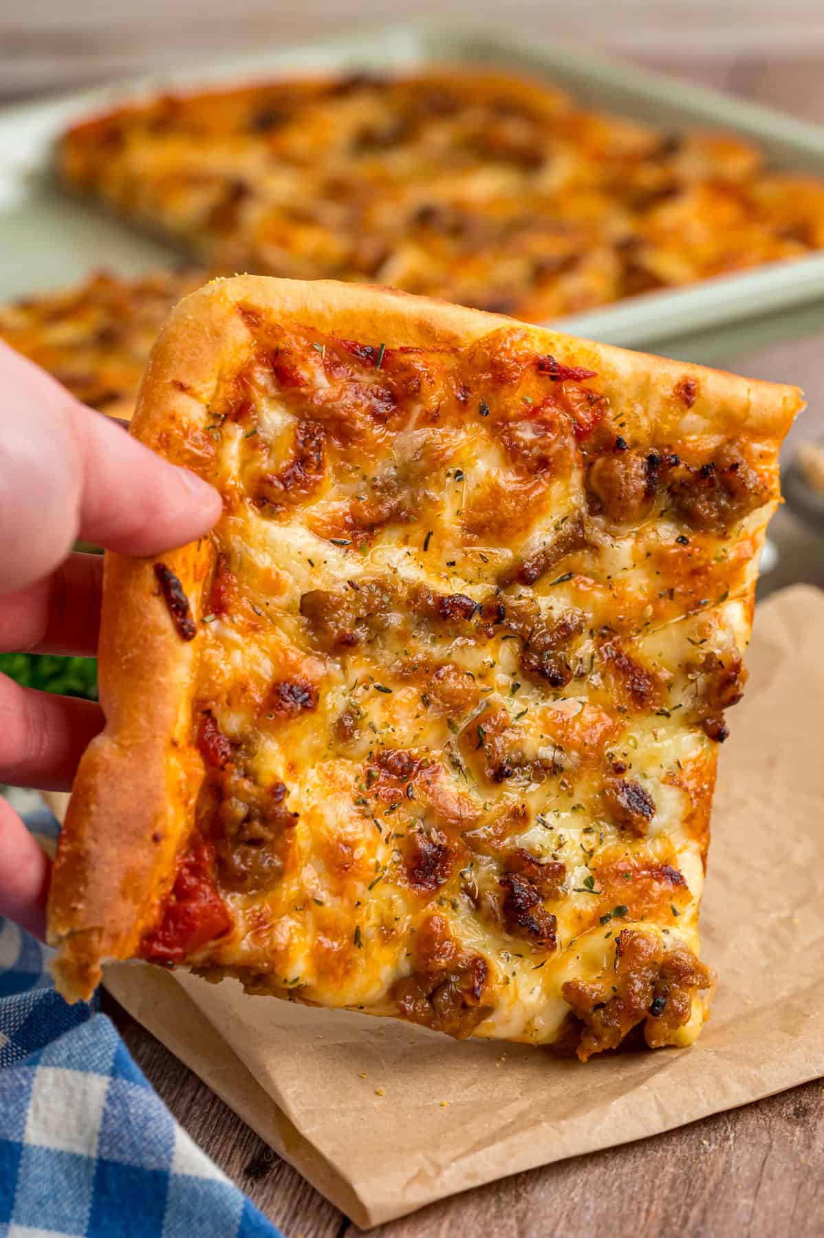 A hand holding a slice of sausage sheet pan pizza
