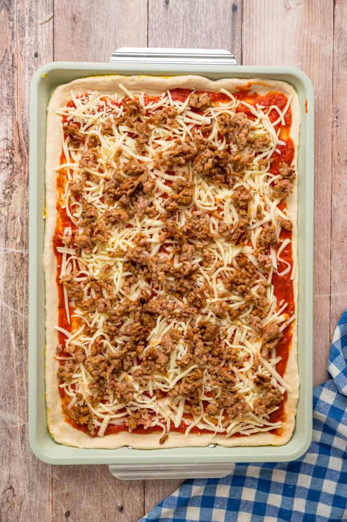 Mozzarella cheese and ground sausage on pizza sauce and dough