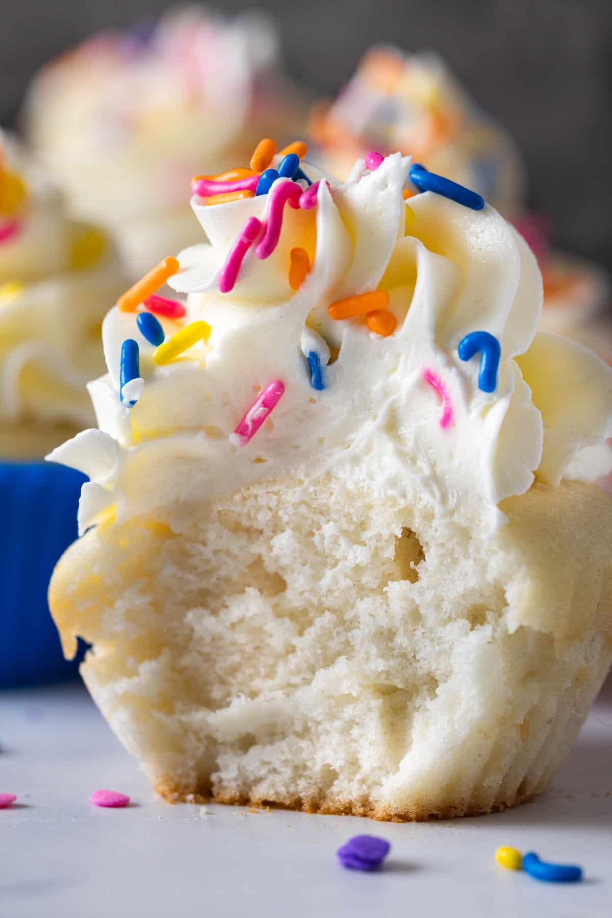 A vanilla cupcake topped with Italian buttercream with a bite missing