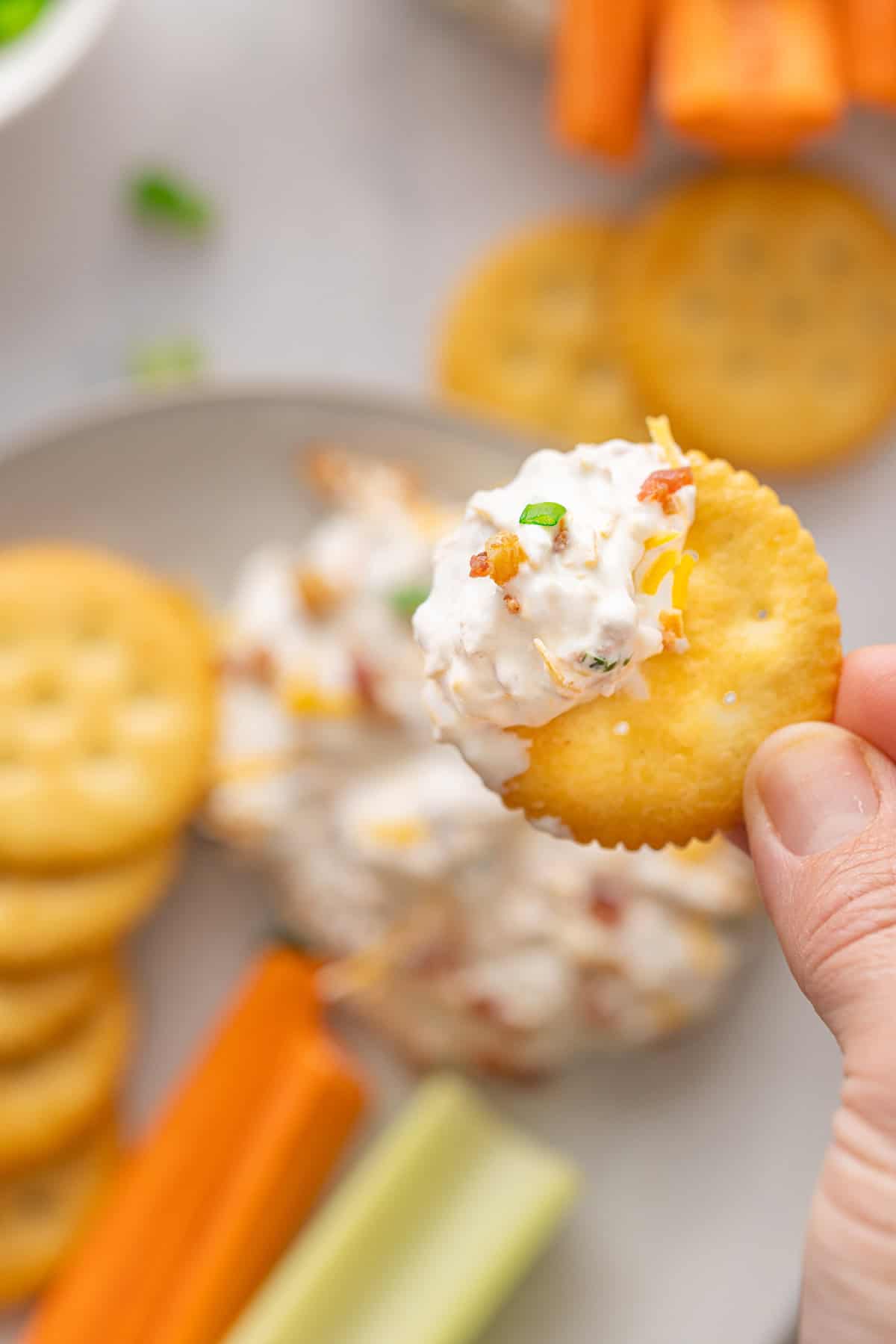 A hand holding a Ritz cracker with million dollar dip