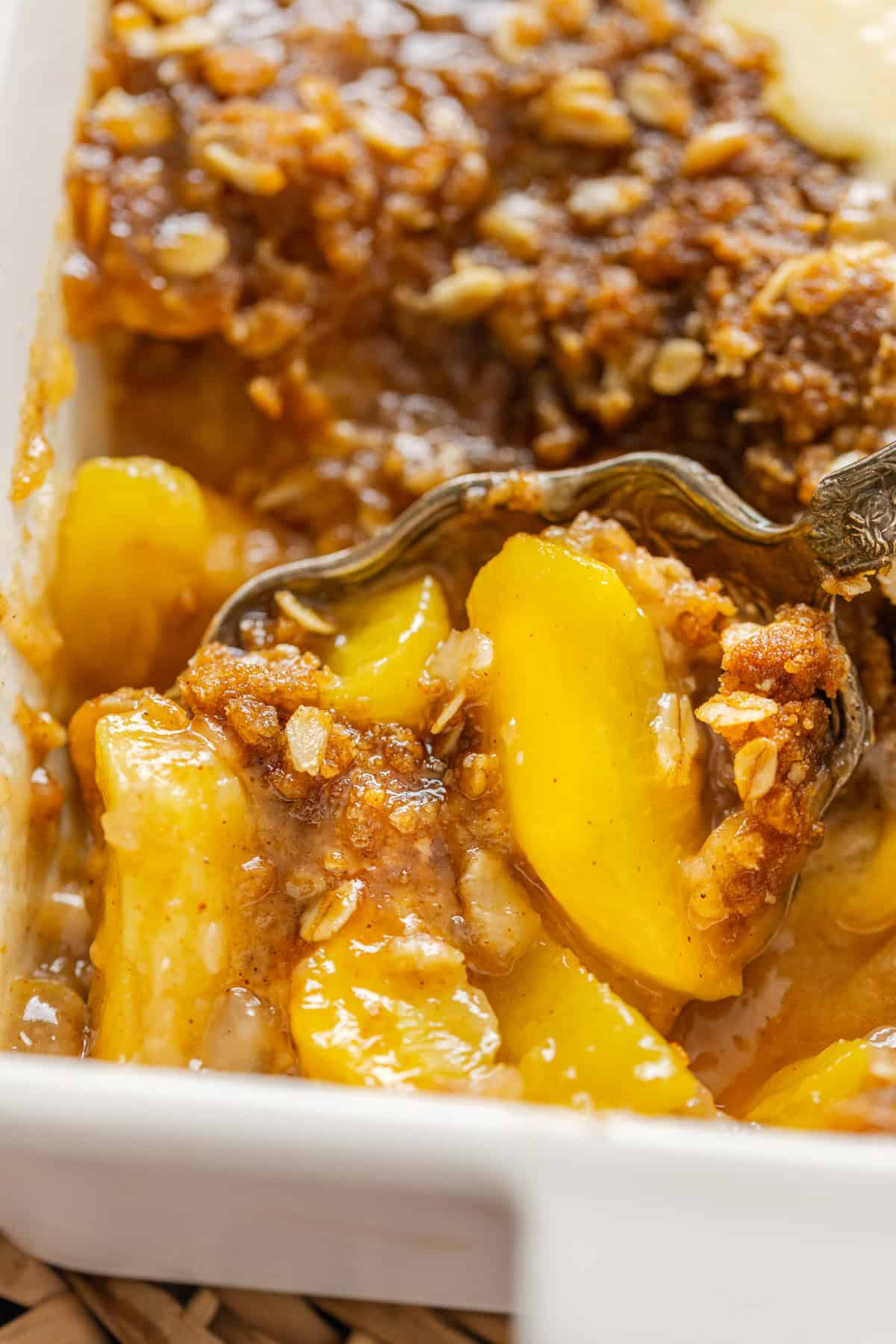 Warmly spiced fresh peaches are topped with a crumble topping in this Peach Crisp recipe. Serve with ice cream for a quick & easy dessert! A spoon in a baking dish of peach crisp