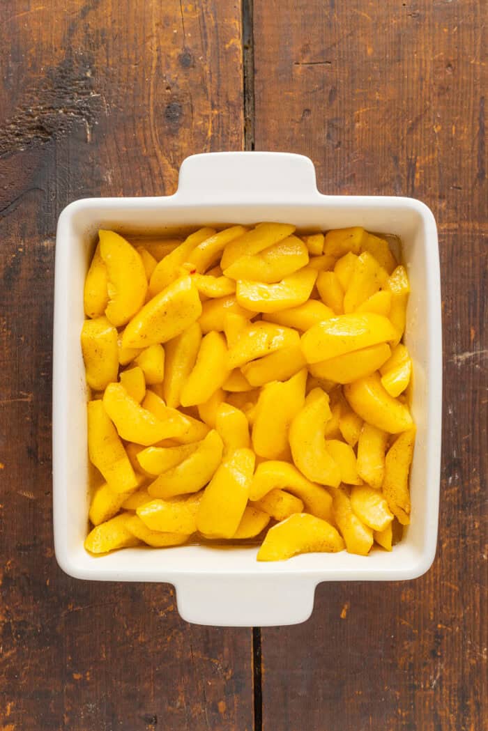 Warmly spiced fresh peaches are topped with a crumble topping in this Peach Crisp recipe. Serve with ice cream for a quick & easy dessert! Overhead view of peaches in a baking dish