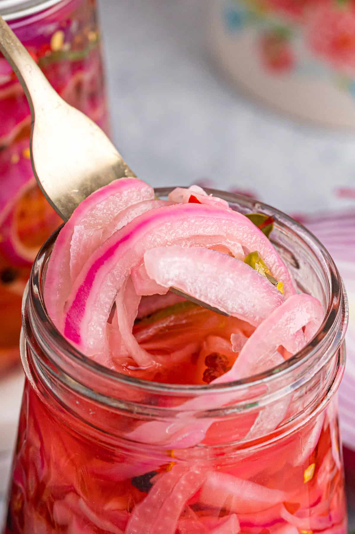A fork pulling quick pickled red onions from a jar