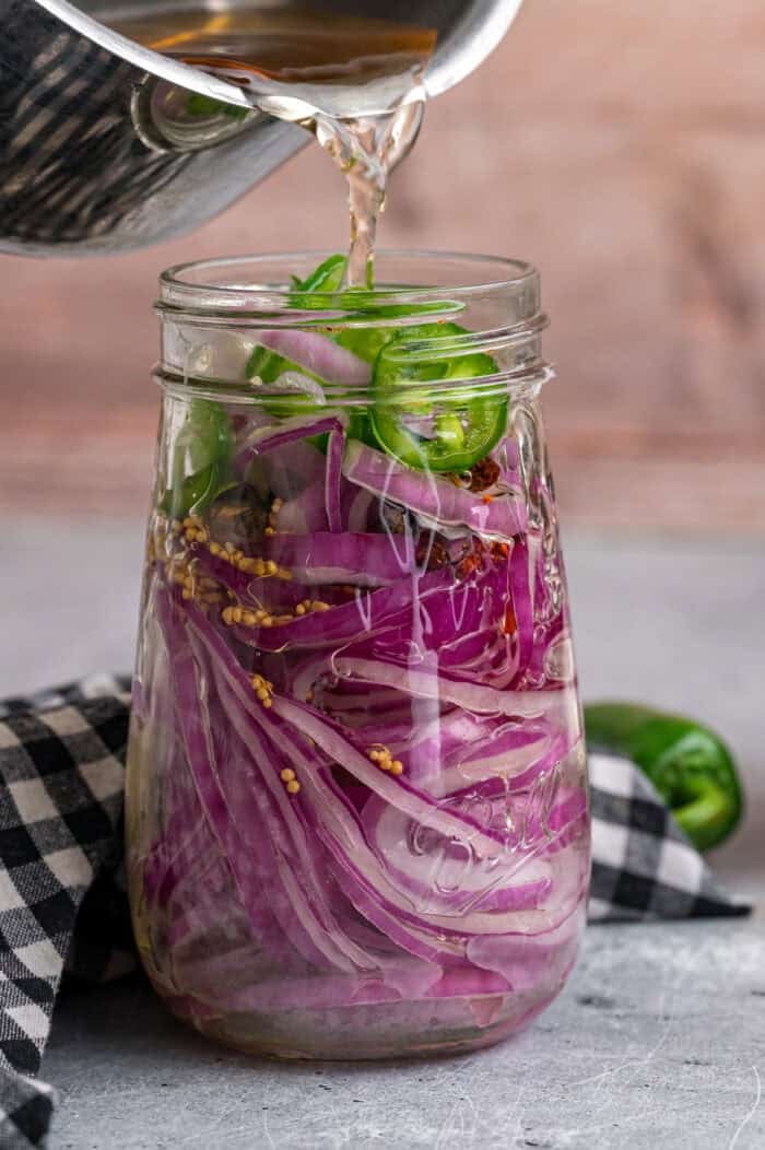Pouring pickling vinegar over red onions in a jar