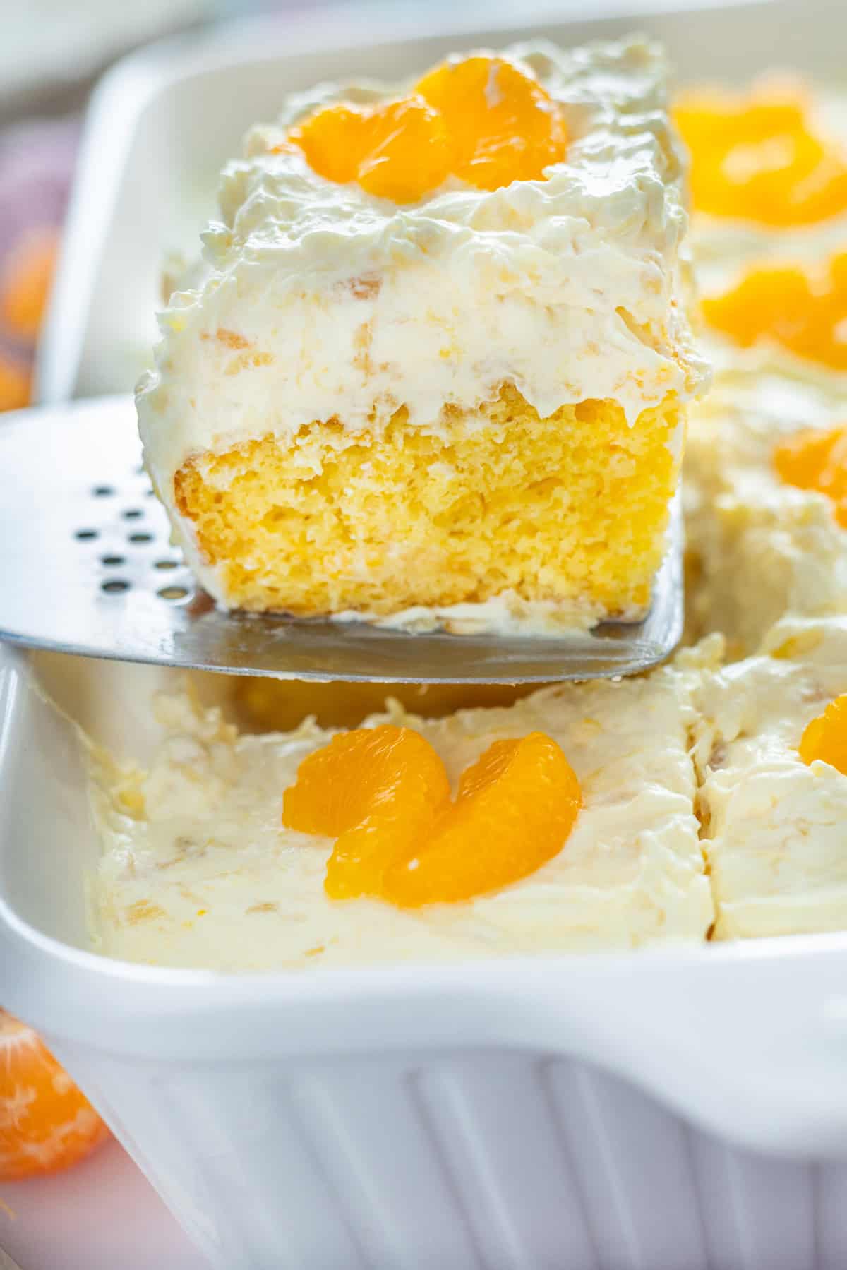 This Pig Pickin' Cake is made with box cake mix combined with mandarin oranges and a pineapple Cool Whip frosting. SO easy to make! Serving a slice of pig pickin' cake