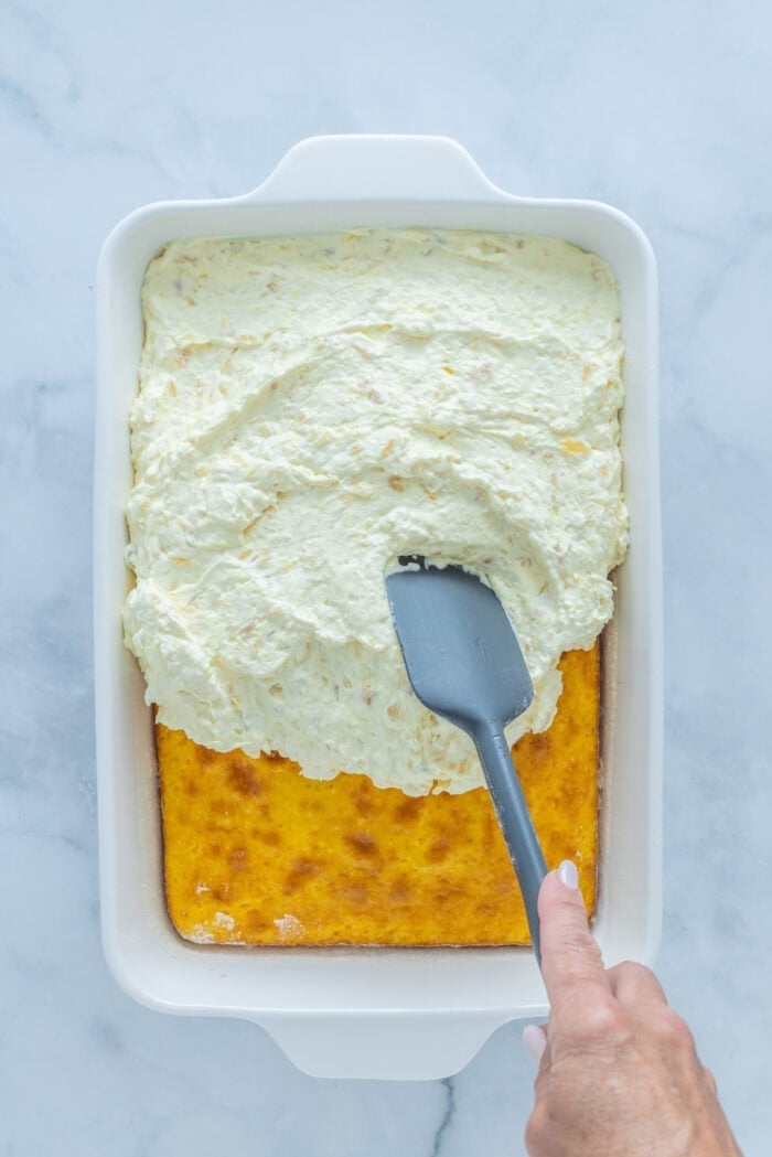 This Pig Pickin' Cake is made with box cake mix combined with mandarin oranges and a pineapple Cool Whip frosting. SO easy to make! Spreading frosting over cake