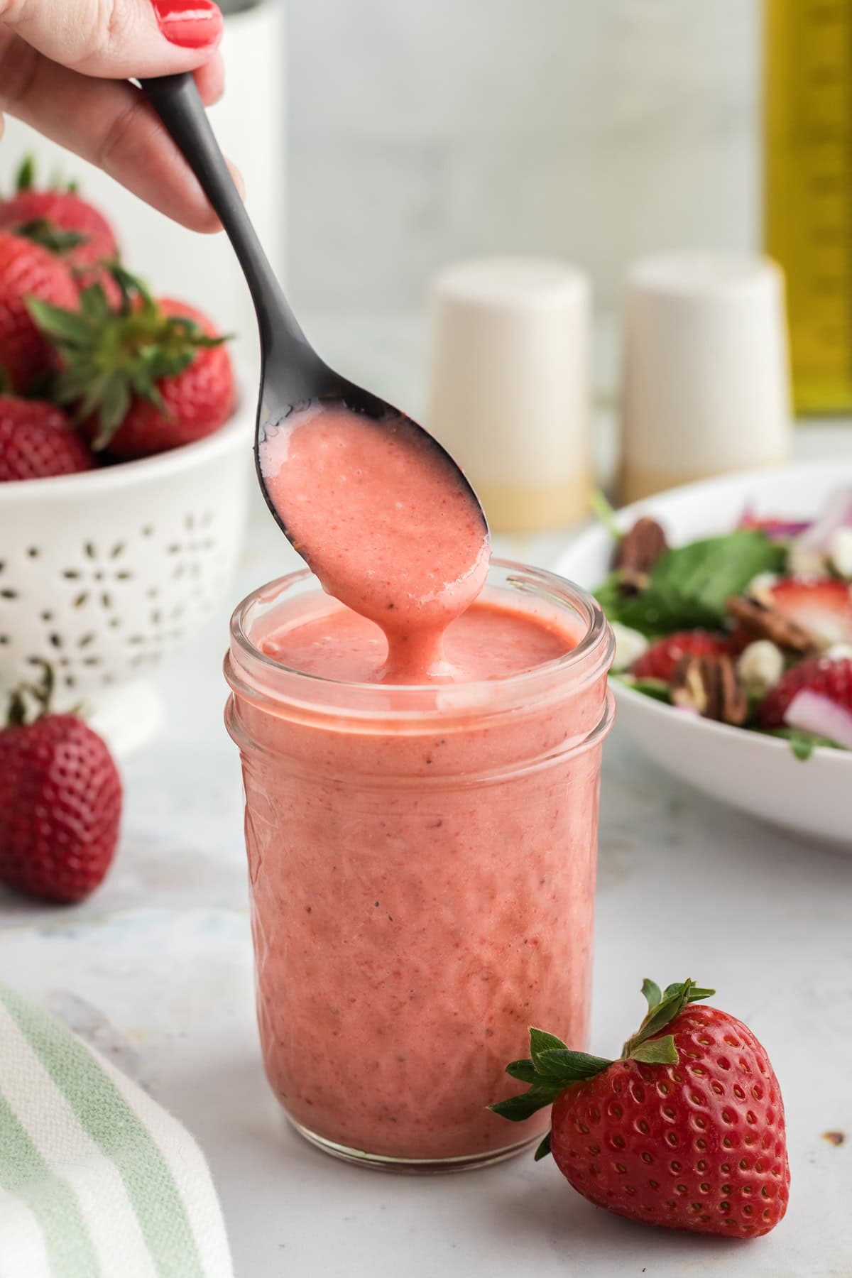 Made with just 4 ingredients in 5 minutes, this Strawberry Vinaigrette is light and tangy with a hint of sweetness. A spoon above a jar of strawberry vinaigrette