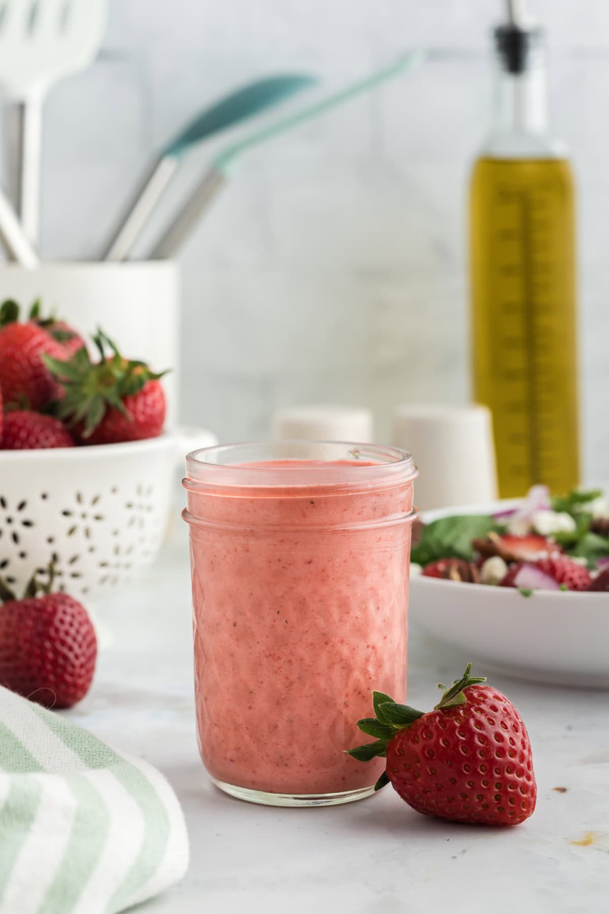 A jar of strawberry vinaigrette in front of a bowl of strawberries
