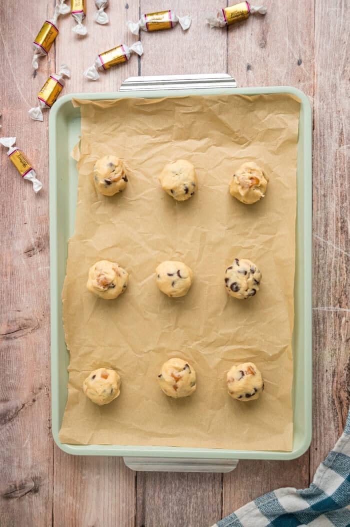 Balls of caramel chocolate chip cookie dough on a baking sheet