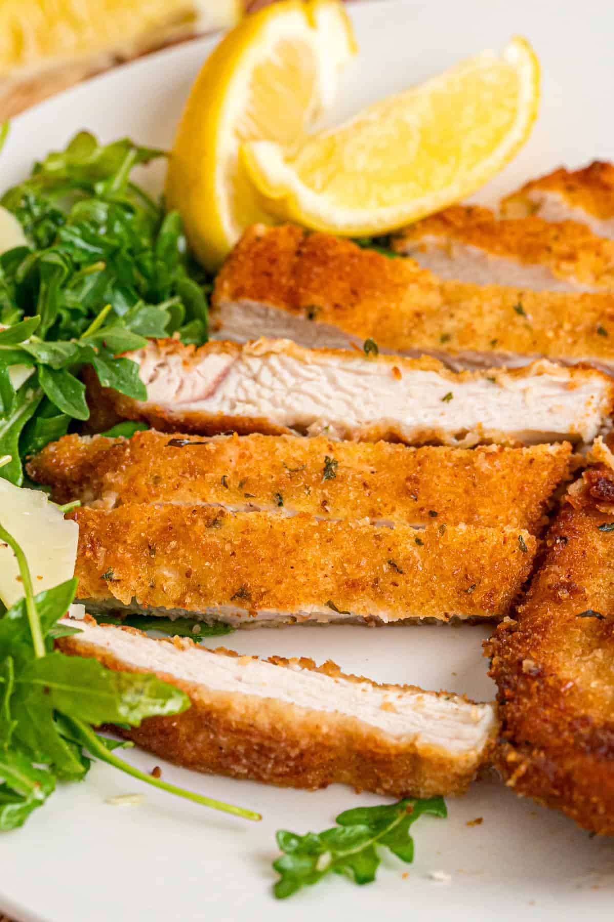 Close up of sliced chicken milanese with lemon wedges