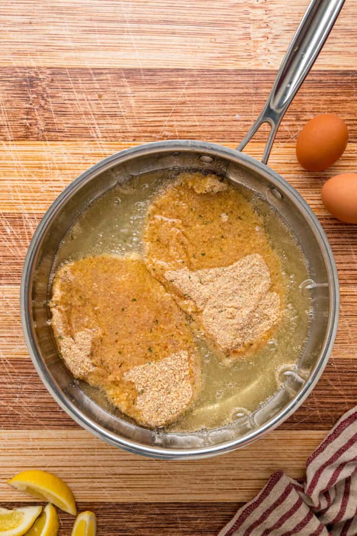 Two chicken cutlets frying in oil