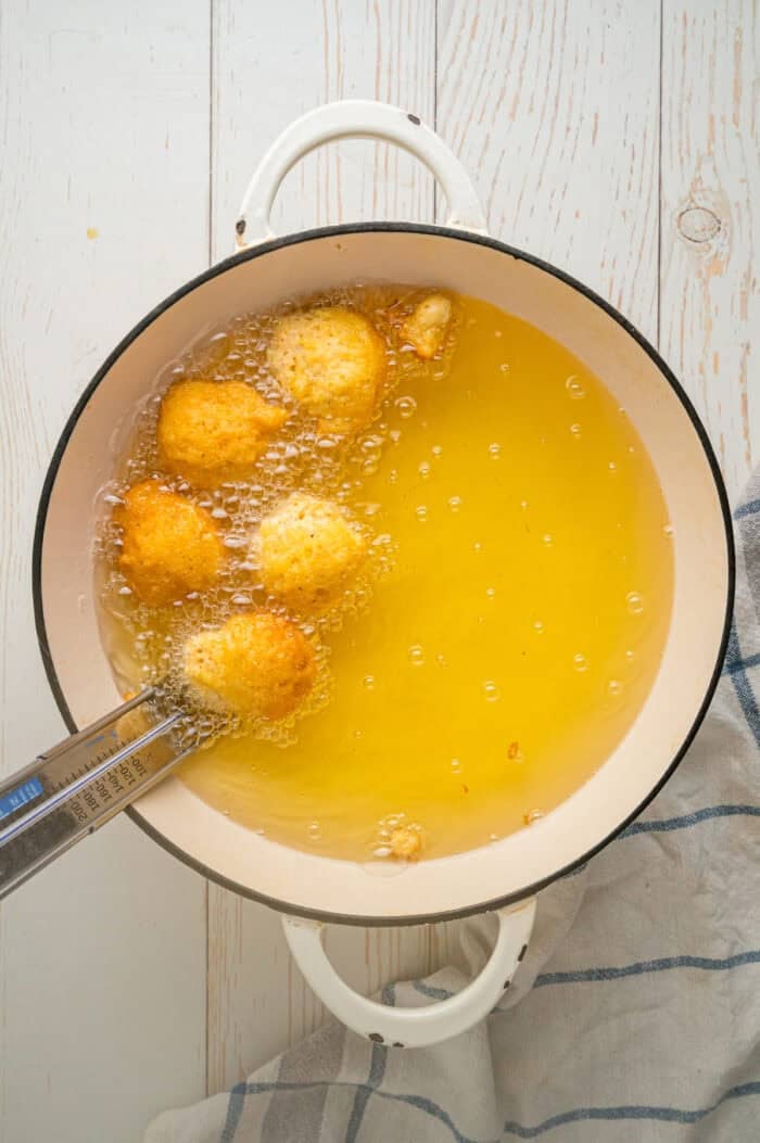 Tongs removing hush puppies from oil
