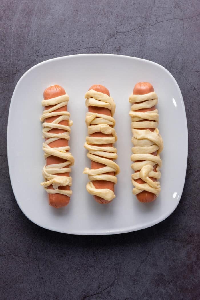 Hot dogs wrapped in crescent roll dough strips on a plate