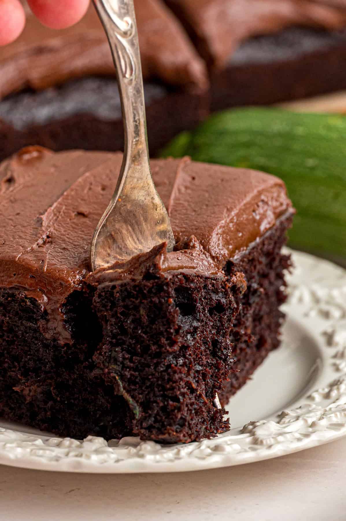 This Chocolate Zucchini Cake is rich, moist, and topped with an irresistible chocolate buttercream! It's a must-bake every summer! A fork in a slice of chocolate zucchini cake