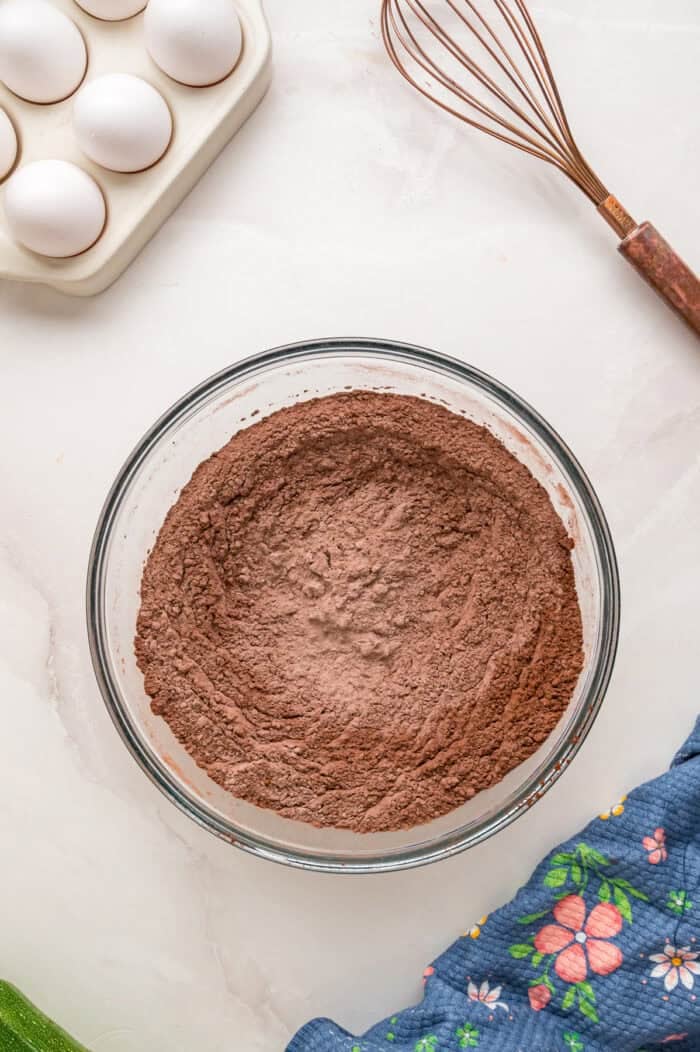 This Chocolate Zucchini Cake is rich, moist, and topped with an irresistible chocolate buttercream! It's a must-bake every summer! Dry chocolate cake ingredients in a bowl