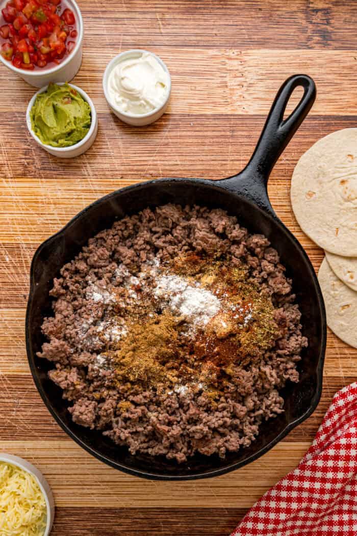 Seasonings added to ground beef in a skillet