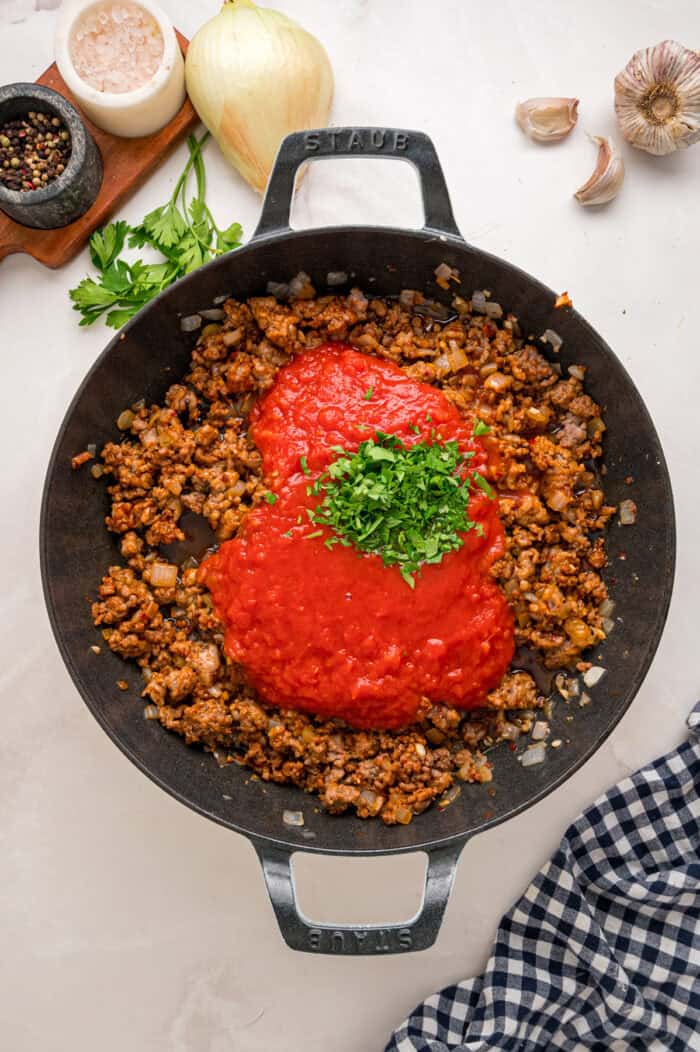 Diced tomatoes and parsley added to ground meat in a skillet