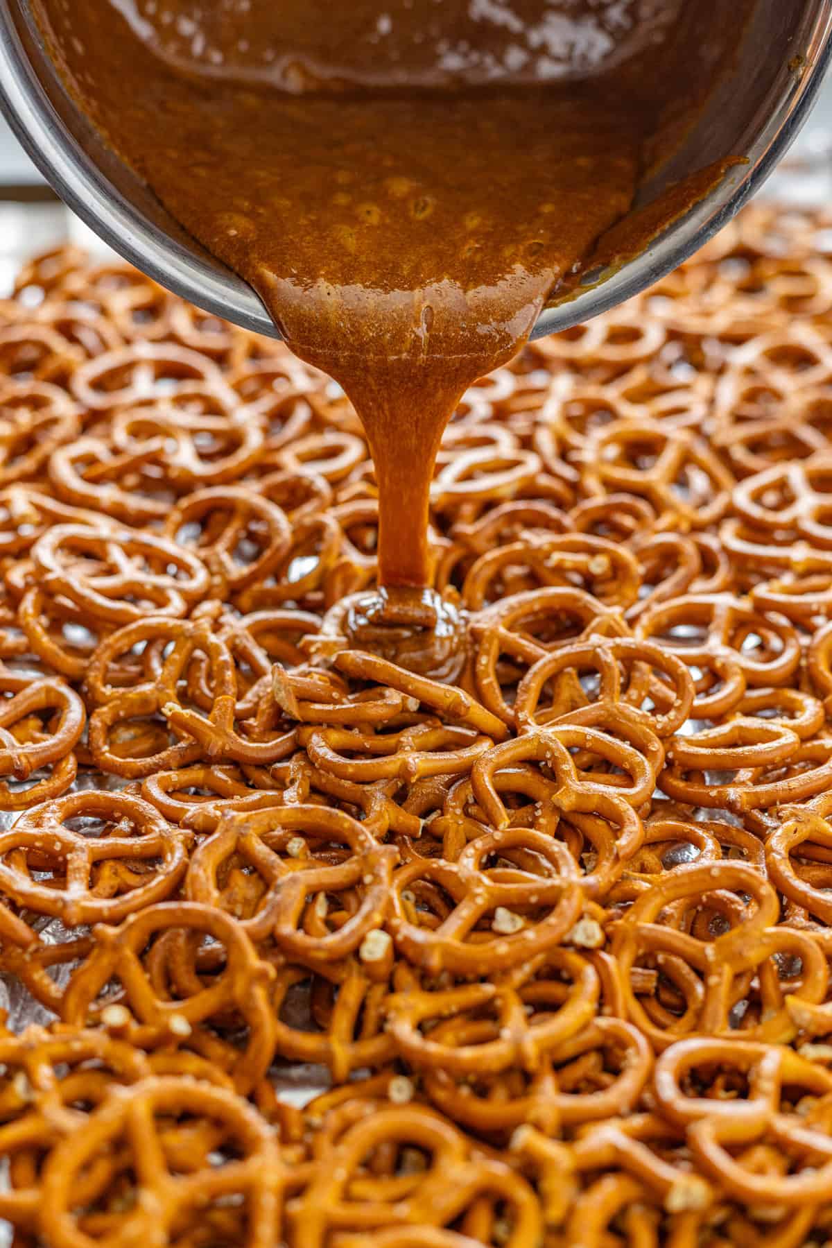 Pouring butter toffee over pretzels on a baking sheet