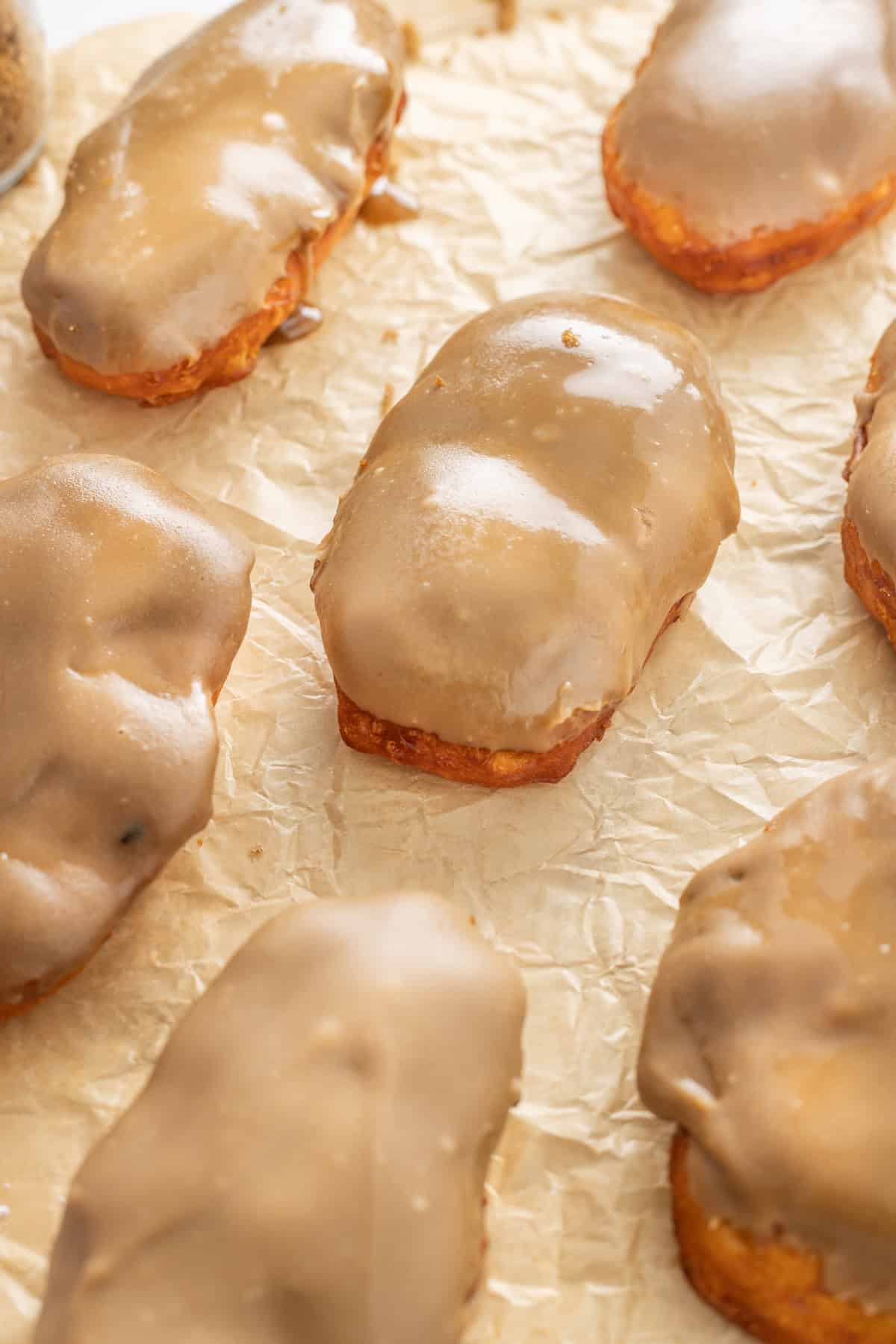 Soft, fluffy fried donuts are topped with a sweet maple frosting in this Maple Bars recipe. Quick & easy to make! Overhead view of maple bars on parchment paper