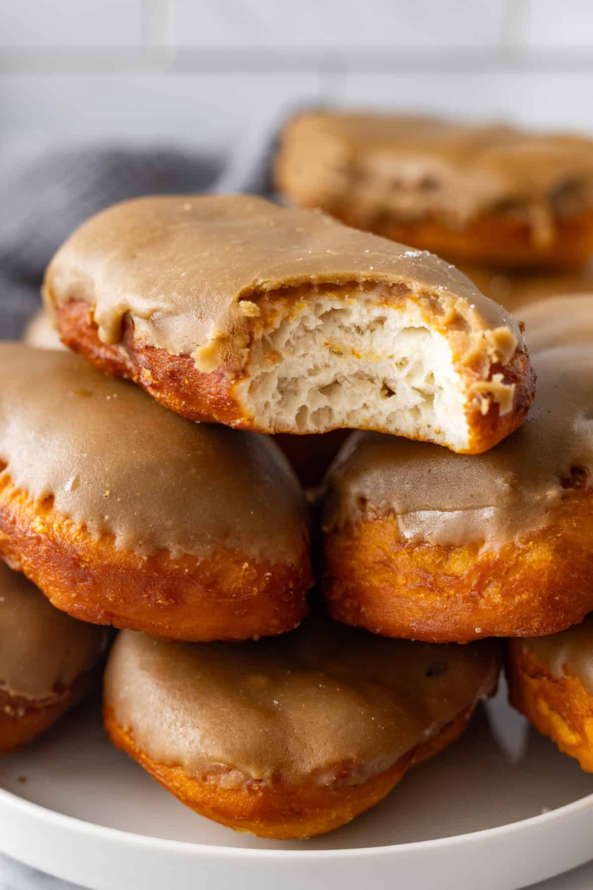 Soft, fluffy fried donuts are topped with a sweet maple frosting in this Maple Bars recipe. Quick & easy to make! A plate of maple bars