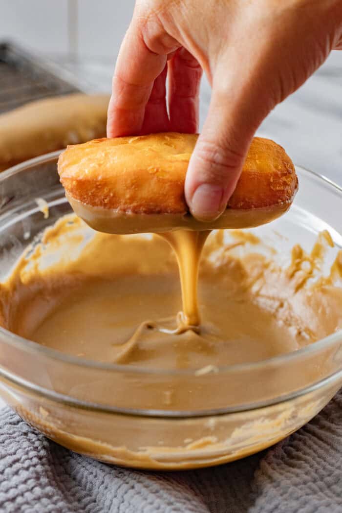 Soft, fluffy fried donuts are topped with a sweet maple frosting in this Maple Bars recipe. Quick & easy to make! Dipping a fried donut into maple glaze
