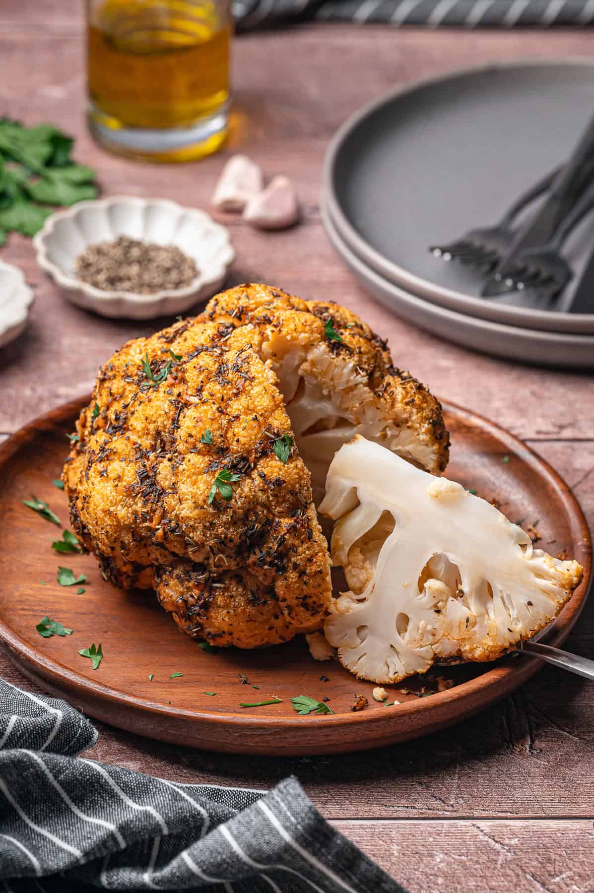 A whole roasted cauliflower on a plate with one piece sliced