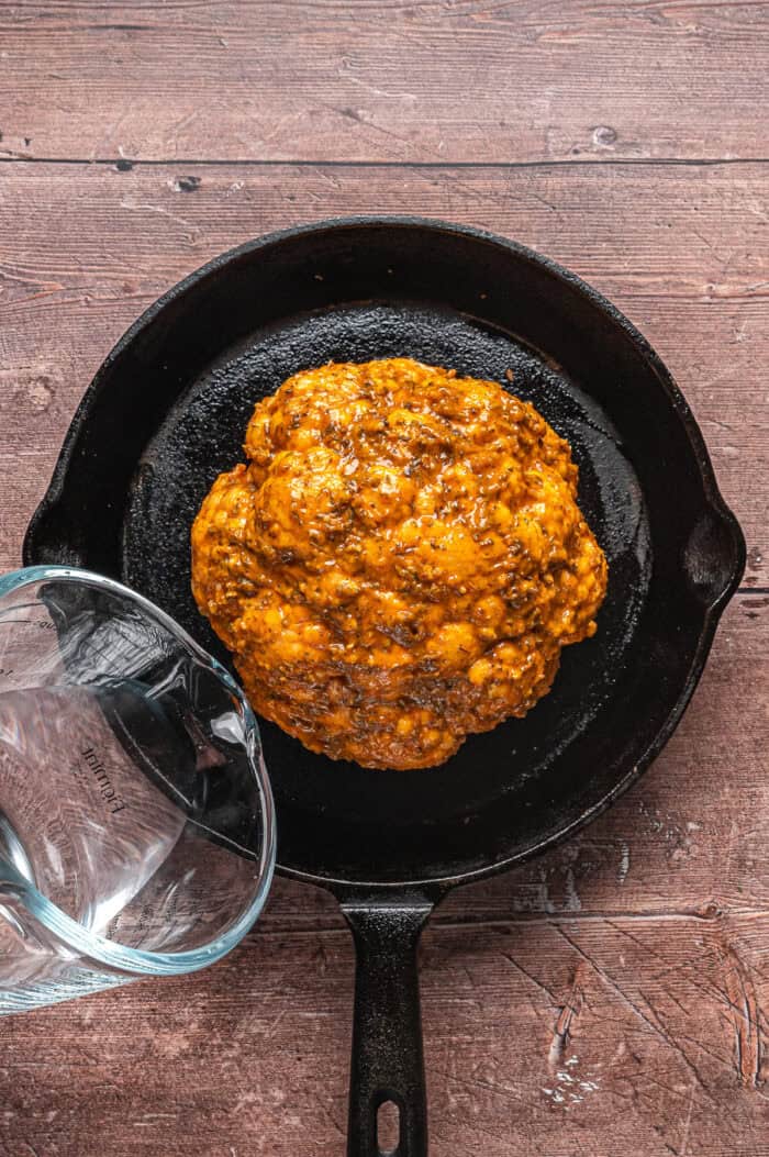 Pouring water in a cast iron skillet with a head of cauliflower