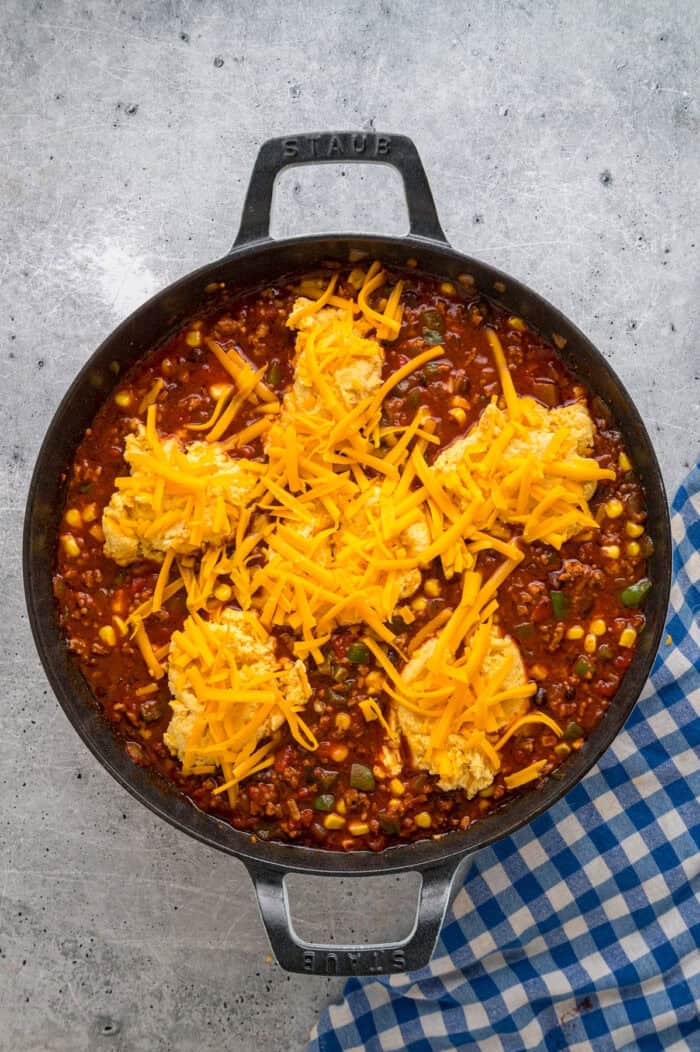 Dollops of cornbread batter and cheddar cheese on chili in a skillet