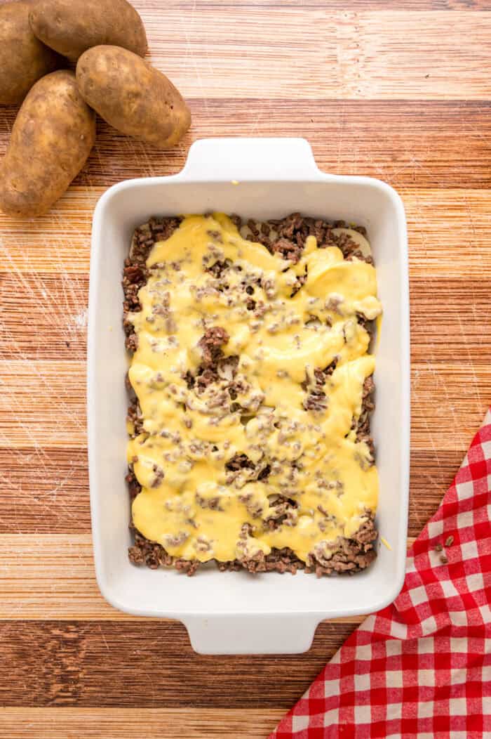 Cheddar cheese soup spread over ground beef in a casserole dish