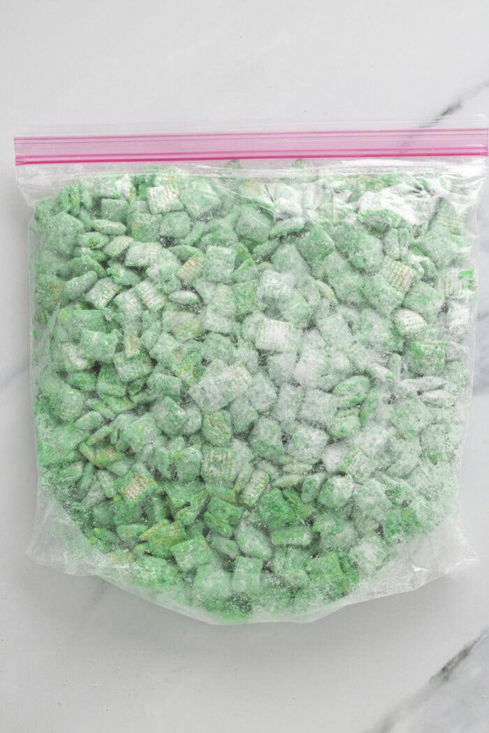 Green chocolate coated Chex cereal in a Ziploc with powdered sugar