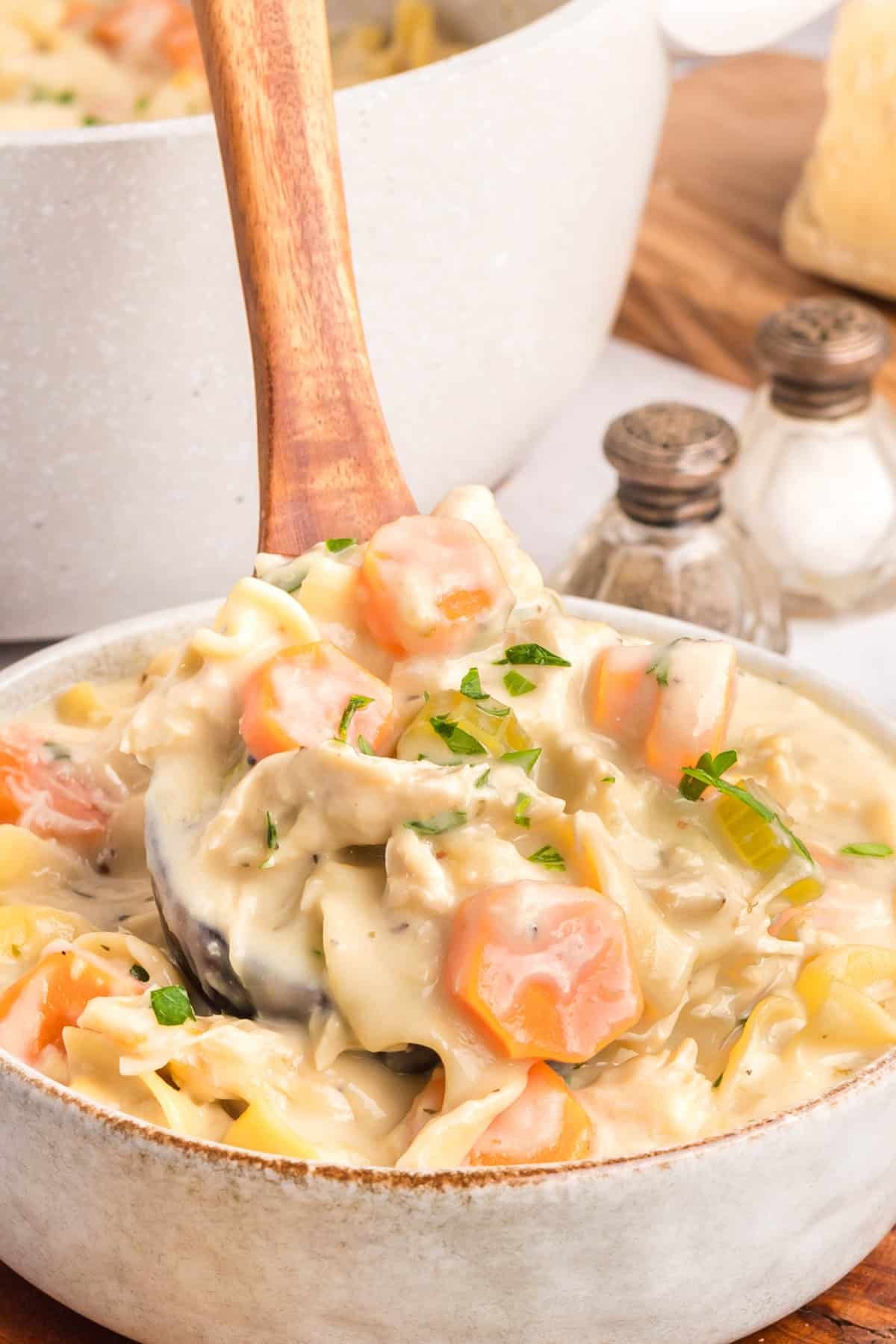 Creamy Chicken Noodle Soup combines tender chicken, hearty noodles, and a flavorful broth in a single pot for a comforting & easy meal. A wooden spoon in a bowl of creamy chicken noodle soup