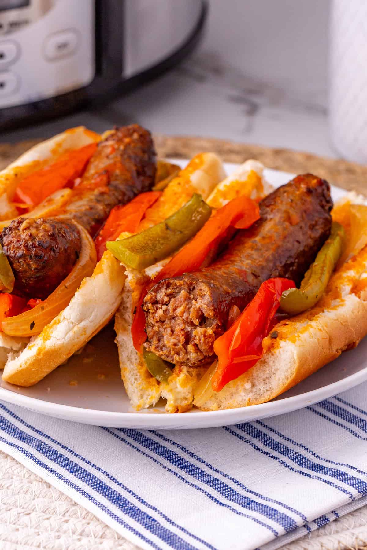 Sausage links, bell peppers, and onions are slow cooked in marinara sauce for an easy dinner in this Slow Cooker Sausage and Peppers recipe. Sausage and peppers on hot dog buns on a white plate