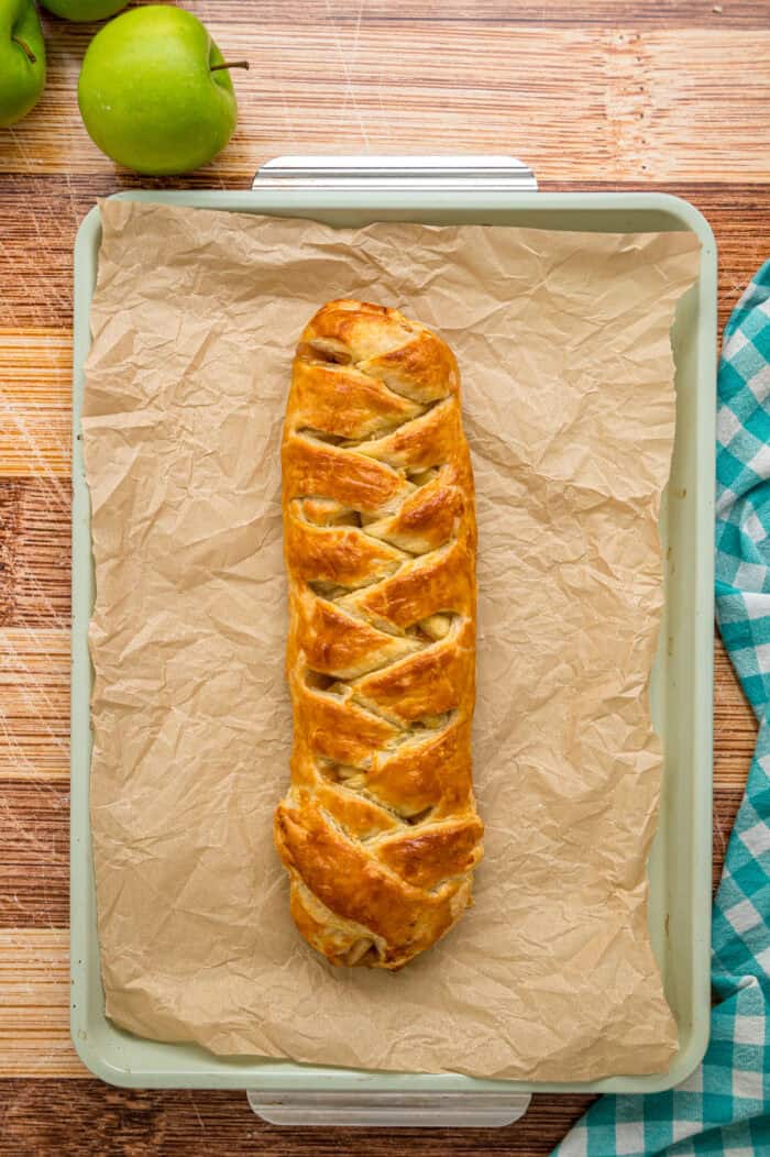 Warmly spiced apple filling is baked inside puff pastry sheets and topped with an irresistible maple glaze in this Apple Strudel recipe. Baked apple strudel on a baking sheet