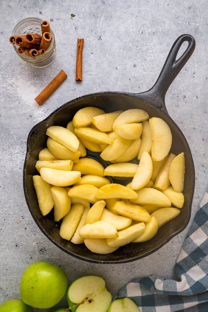 These Southern Fried Apples are warmly spiced, tender, and coated in a yummy brown sugar syrup. Enjoy with ice cream! Sliced apples in a cast iron skillet