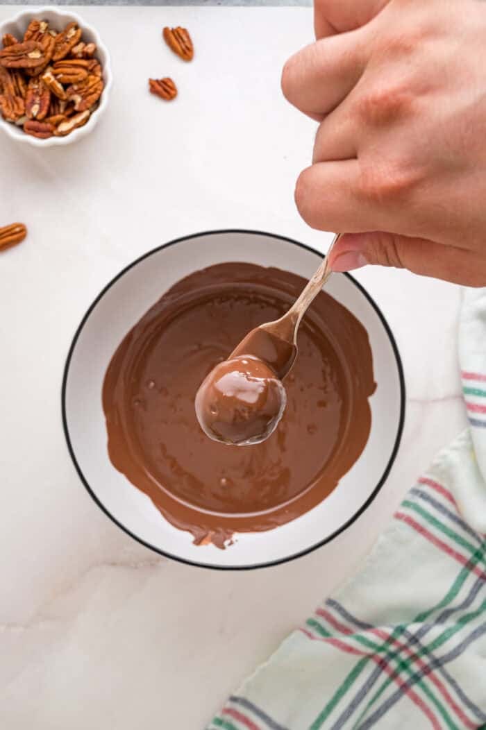 A pecan ball dipped in chocolate on a fork