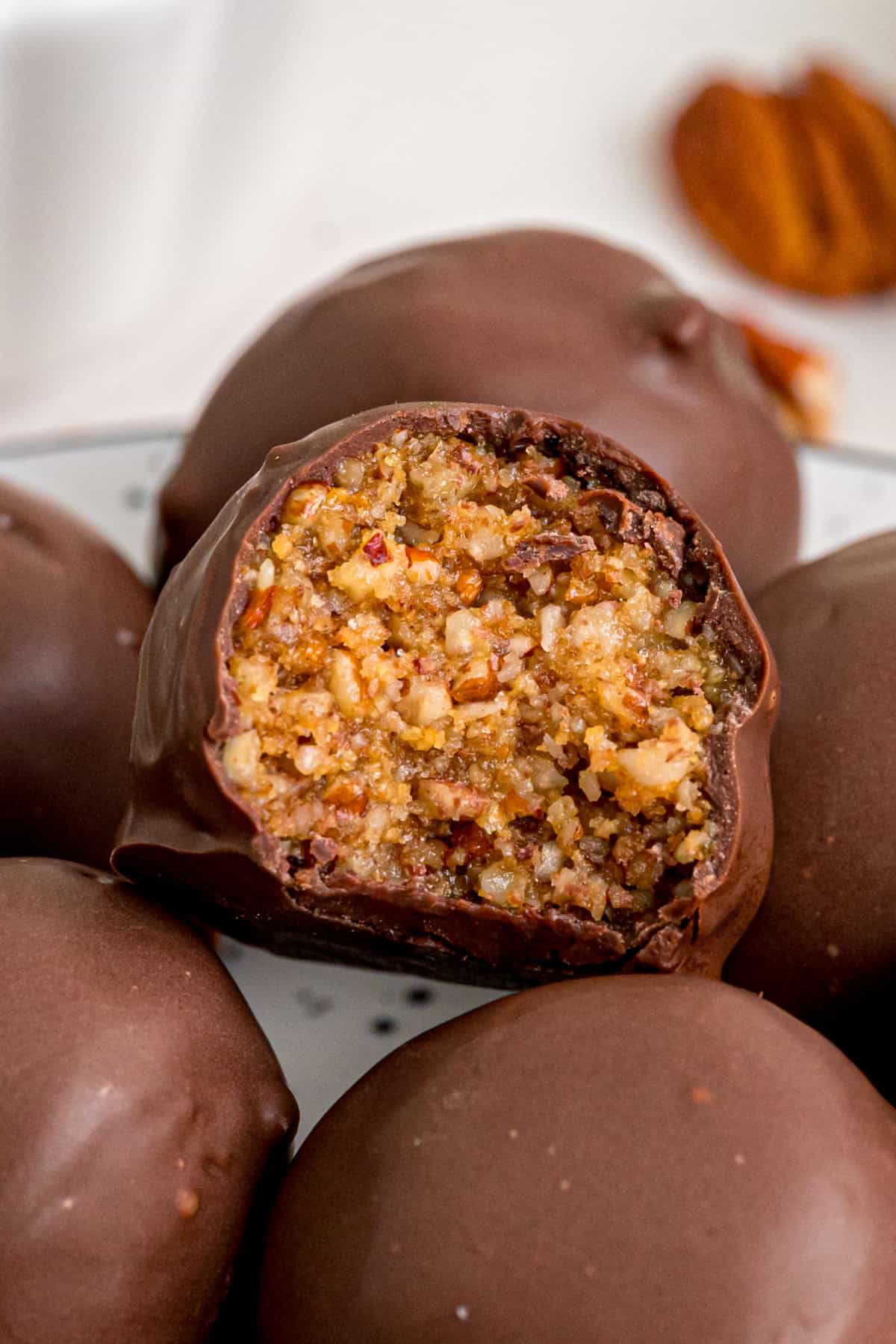 Pecan Pie Balls are a no-bake treat dipped in chocolate that taste just like pecan pie! Add sprinkles to give them a festive flair. A plate of pecan pie balls, one showing the inside