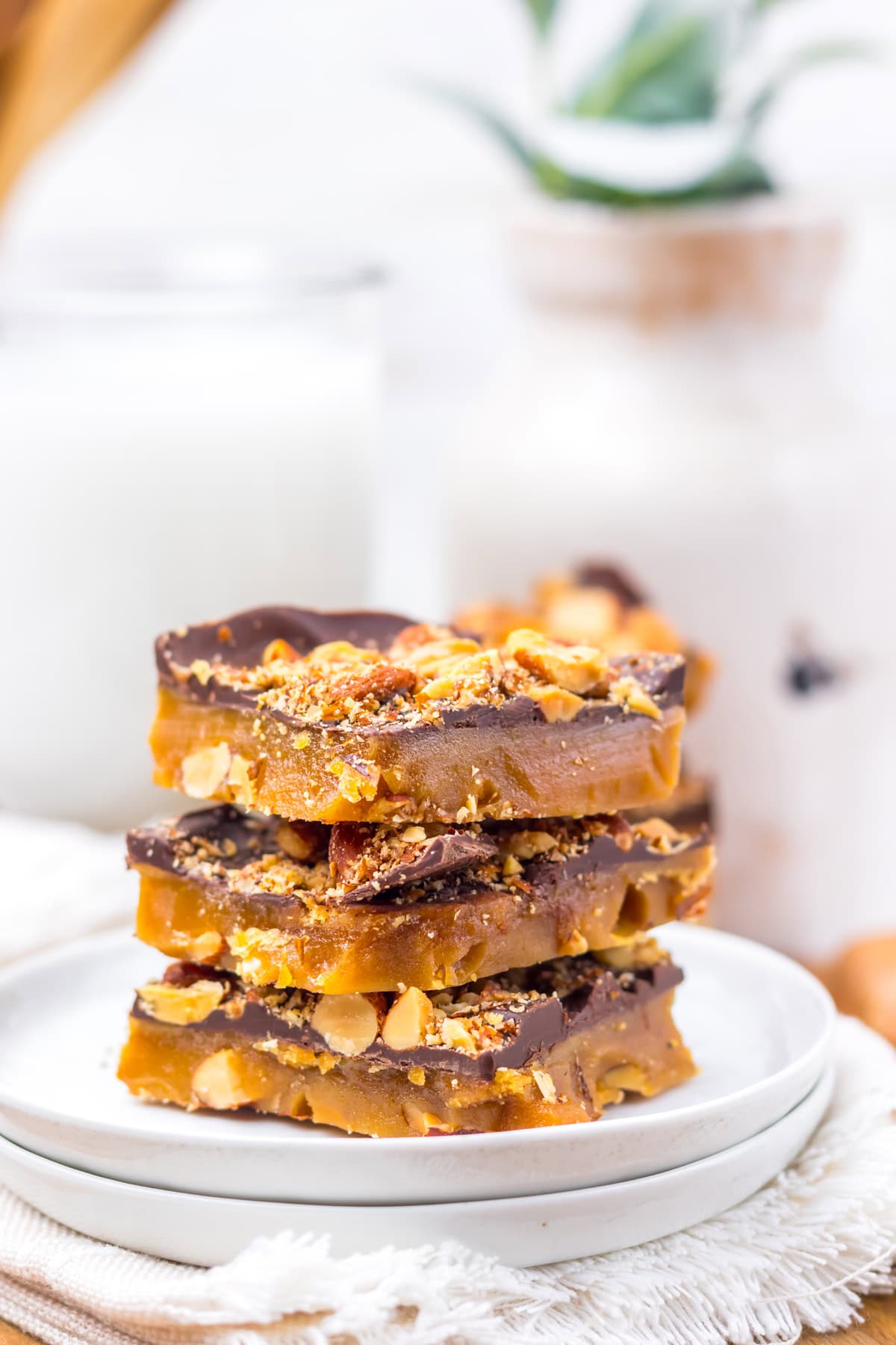 With just four ingredients, this Almond Roca Recipe features layers of almonds, toffee, and chocolate. Buttery, crunchy, and easy to make! Three pieces of almond roca on a white plate