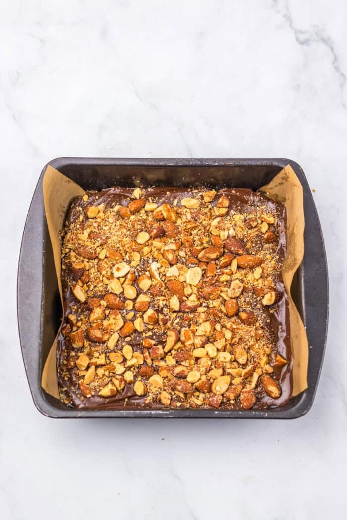 With just four ingredients, this Almond Roca Recipe features layers of almonds, toffee, and chocolate. Buttery, crunchy, and easy to make! Finished almond roca recipe in a square pan