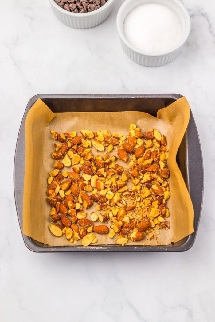 With just four ingredients, this Almond Roca Recipe features layers of almonds, toffee, and chocolate. Buttery, crunchy, and easy to make! Sliced toasted almonds in a square baking pan