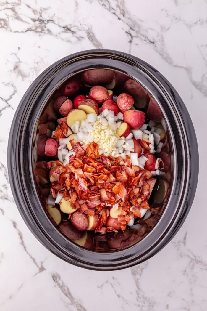 Halved baby potatoes, ranch seasoning, and bacon in a crockpot.
